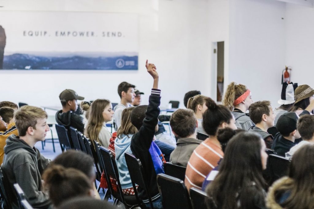 Person wearing black jacket raising hand in classroom